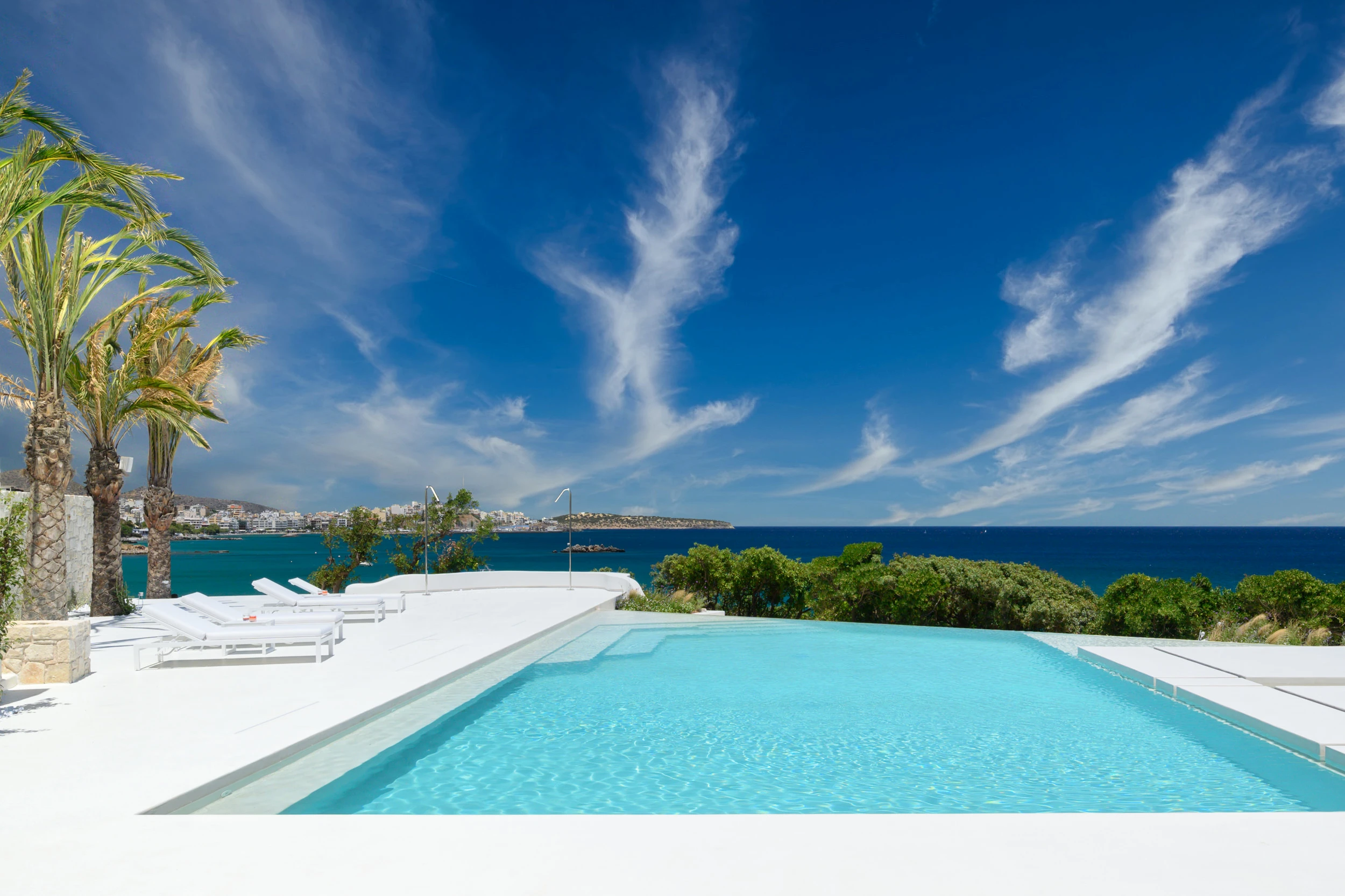 Η πισίνα στο The Island Concept στην Κρήτη, με λευκές βεράντες, θέα στη θάλασσα και εντυπωσιακούς σχηματισμούς νεφών.