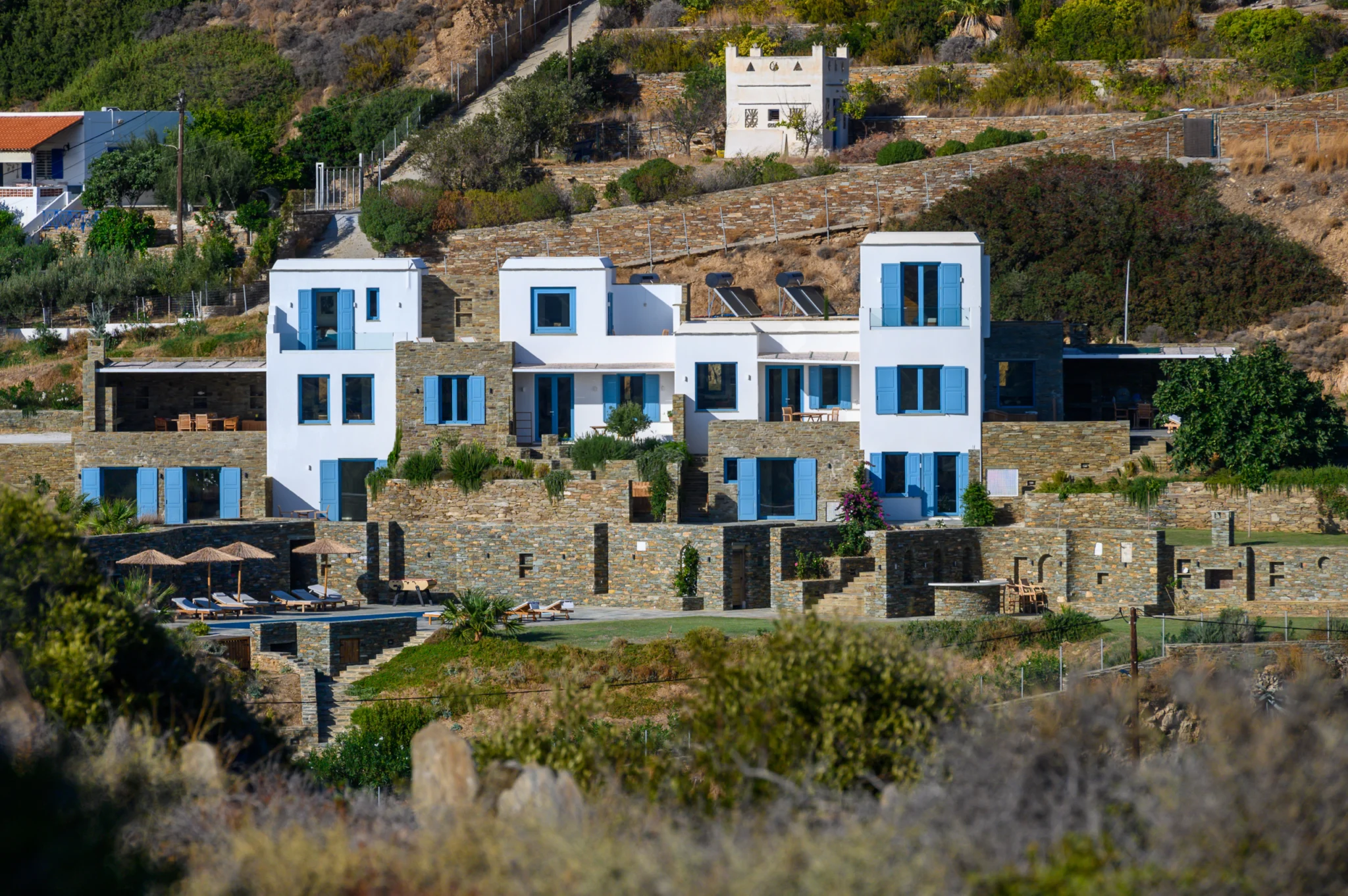 Λευκα κτιρια με μπλε παραθυροφυλλα και πετρινες βεραντες στην πλαγια