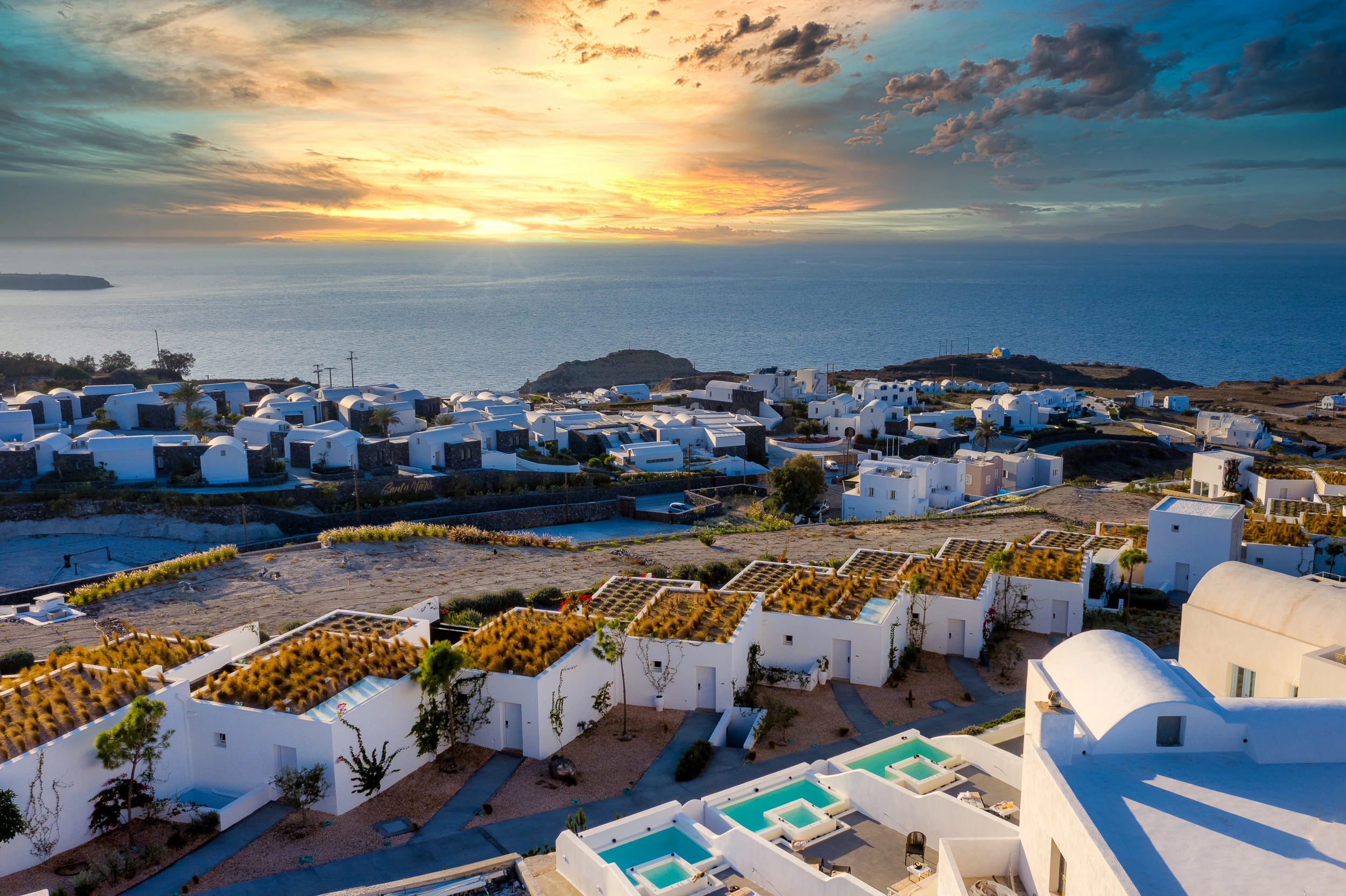 Εναέρια άποψη του Santolia Art Boutique Suites και του οικισμού της Σαντορίνης στο ηλιοβασίλεμα.